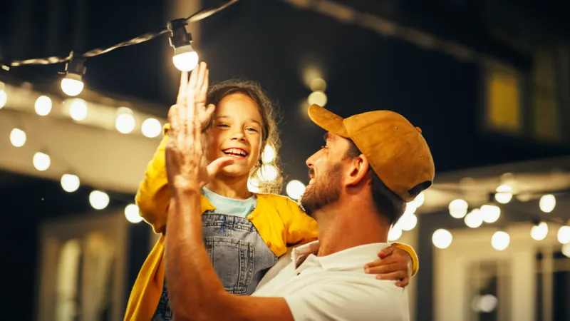 proud handsome father helping his little beautiful daughter to change a lightbulb in fairy lights backyard installation at home father and daughter high five and celebrate successful fix