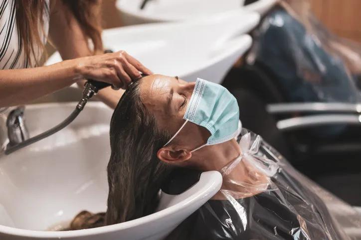 woman hairdresser coiffeur washing female clients hairs in times of coronavirus, woman with eyes closed and mask relaxing, shallow focus