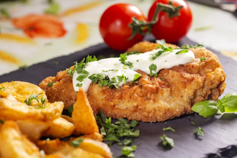 pork schintzel with a white sauce, fries and herbs on a dark slate