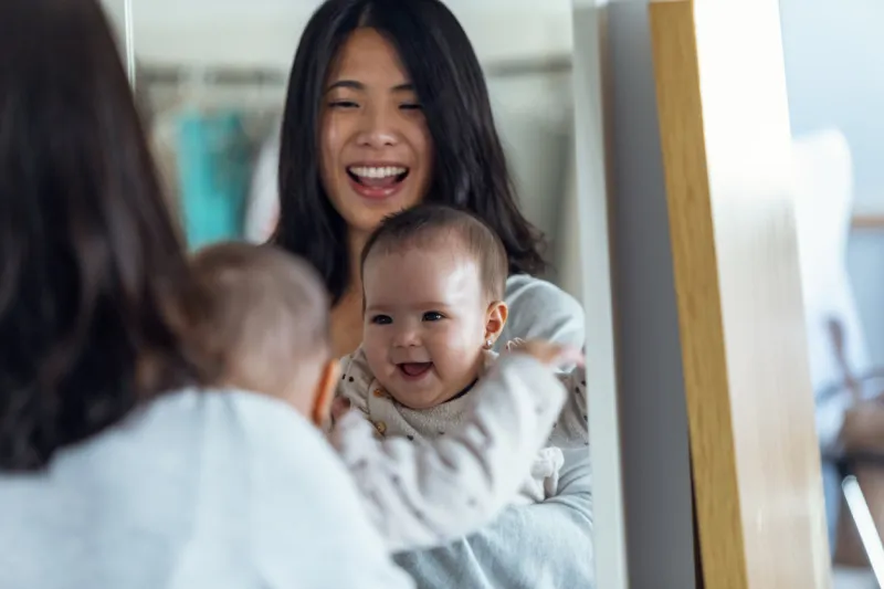 shot of happy young mother with her little girl looking in the mirror while smiling at home