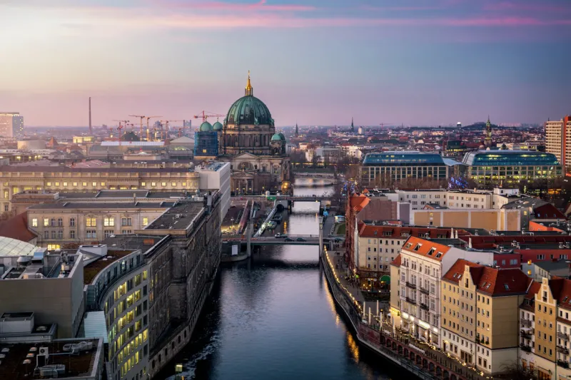 view along the river spree to the berlin cathedral and urban skyline of berlin, germany, with city lights and soft sunset sky