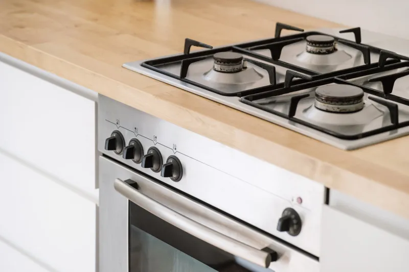 stainless steel gas cooker built in wooden countertop and electric oven with control panel at contemporary kitchen