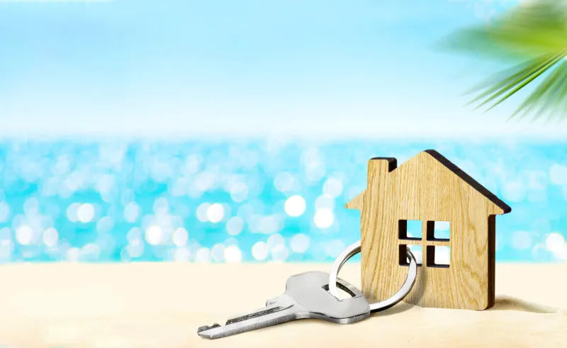 model of house and key on sandy beach with sea and sky on the background