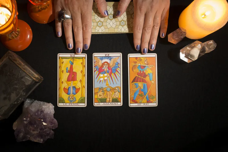detail of a woman's hands showing three tarot cards face up, on a black card table concept of divination session with tarot cards view from above
