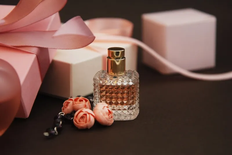 women's pink perfume in beautiful bottle and artificialt flowers bracelet on brown background with gift boxes on background