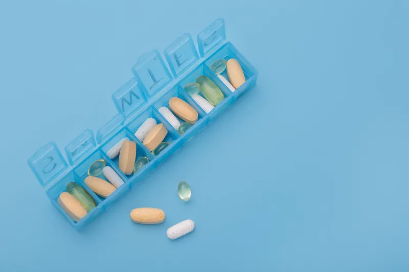 organizer for pills, vitamins and dietary supplements on a light blue background health maintenance concept