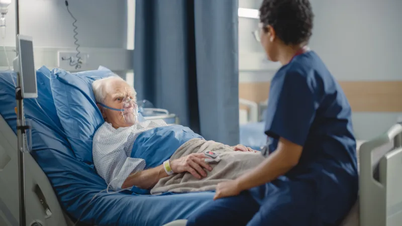 hospital ward  friendly head nurse connects finger heart rate monitor or pulse oximeter to elderly patient wearing oxygen mask resting in bed nurse does patient checkup after successful surgery