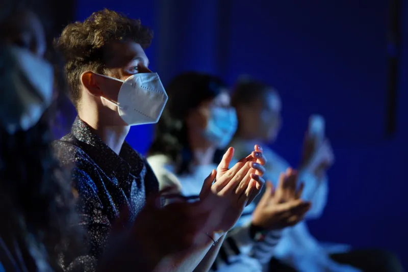 a group of people clapping while listening to presentation at conference, coronavirus concept