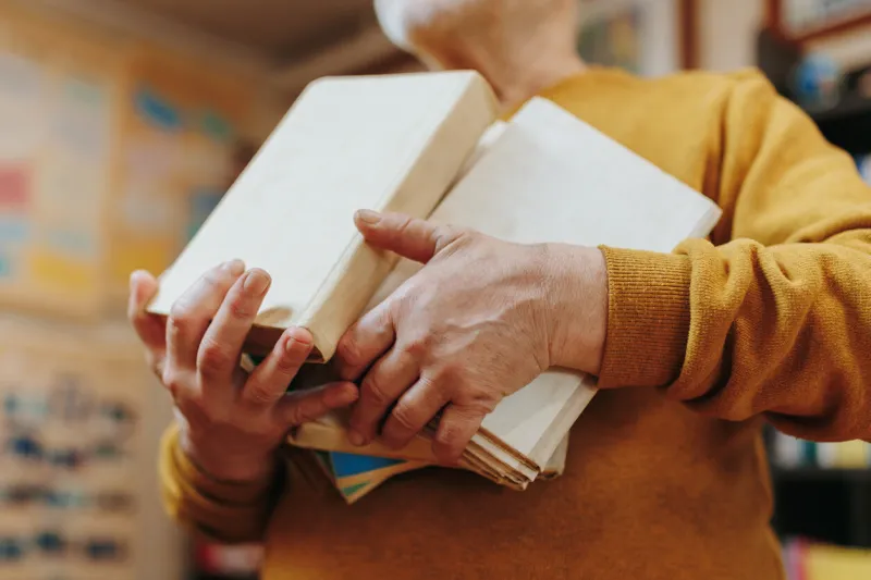this detailed image offers a close-up view of the hands of a senior man as they rest beside a book, capturing the nuanced texture and character of aging hands in exquisite detail