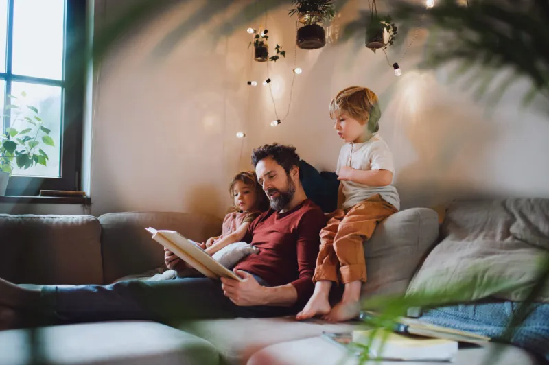 a mature father with two small children resting indoors at home, looking at photo album