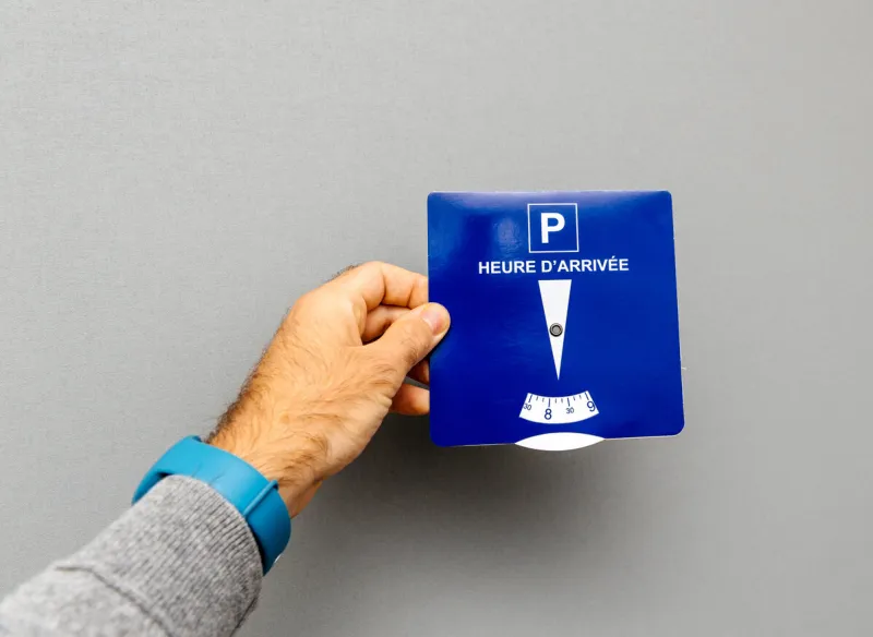 point of view of man holding disk parking with french text heure d'arrivee translated as arrival time from french language - gray background