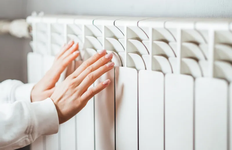 woman warms up hands over heater concept of the need for good central heating