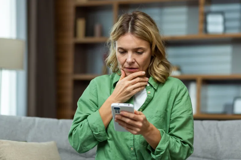 close-up photo worried senior woman mother sitting on sofa at home and holding phone worries about children, writes and sends messages, calls, searches, waits at home