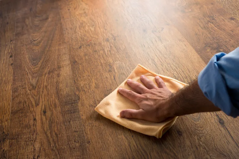 male hand cleaning and rubbing an hardwood floor with a microfiber cloth