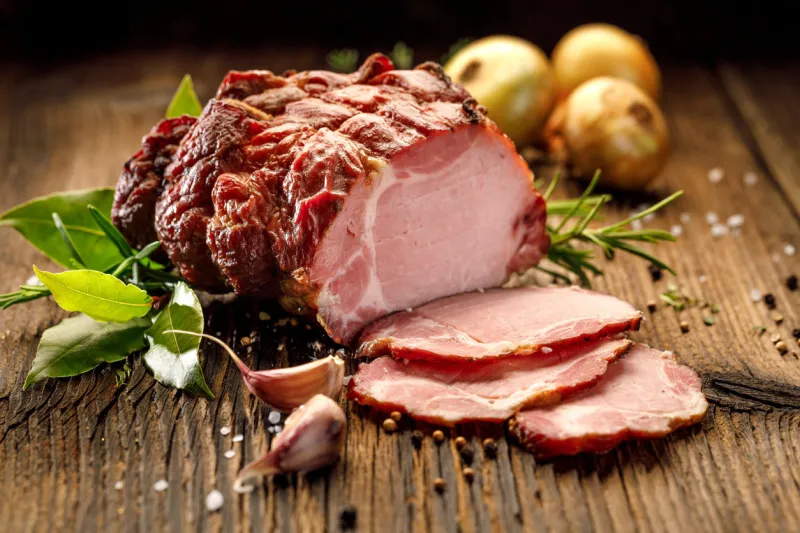 sliced smoked gammon on a wooden table with addition of fresh herbs and aromatic spices  natural product from organic farm, produced by traditional methods