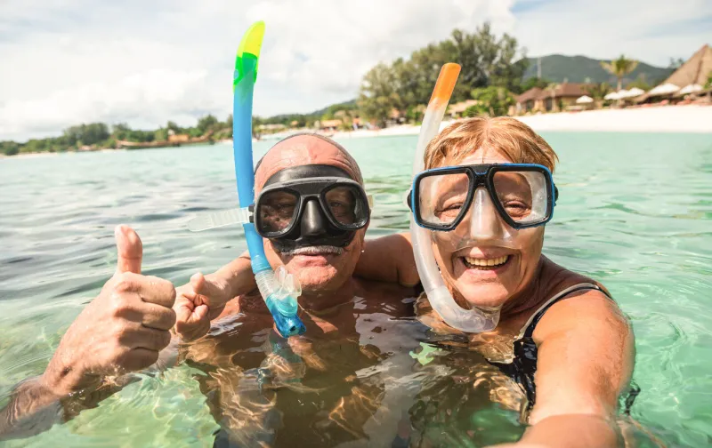 senior happy couple taking selfie in tropical sea excursion with water camera - boat trip snorkeling in exotic scenarios - active retired elderly and fun concept around the world - warm bright filter