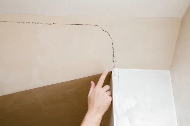 man's hand finger pointing to the cracked wall in house building problems and solutions concept