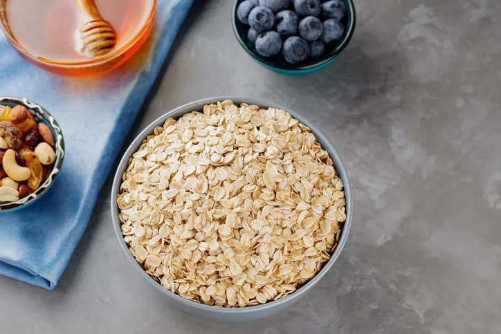 healthy breakfast oatmeal with berries, nuts and honey oat flakes, blueberries, honey and assorted nuts on a gray background vegan breakfast with oatmeal top view
