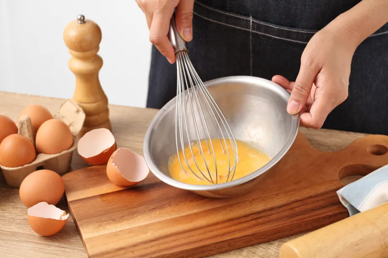 young woman cooking omelet on wooden table