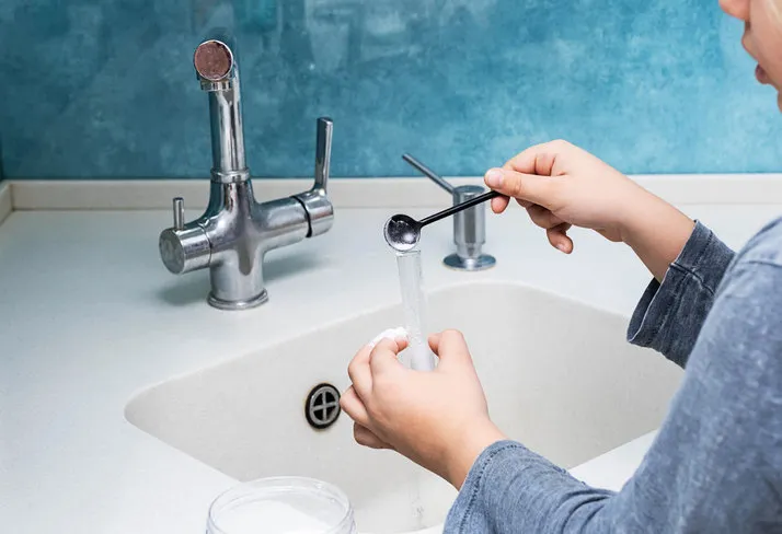 cropped image of unrecognisable boy making experiments with vinegar and baking soda at kitchen science education, playing at home