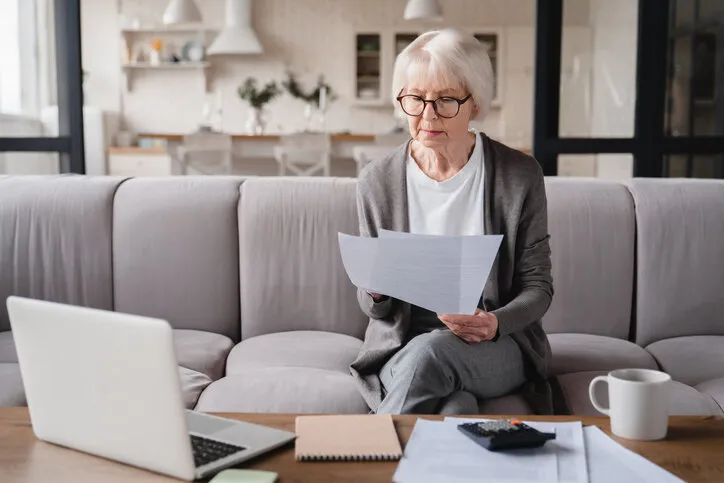old elderly senior caucasian freelancer woman grandmother checking pension documents, loan, e-banking, doing paperwork with laptop, mortgage, paying domestic bills at home