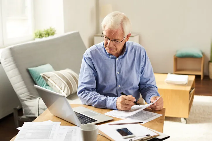 portrait of modern senior man filling in application form at home sitting at table with laptop in living room