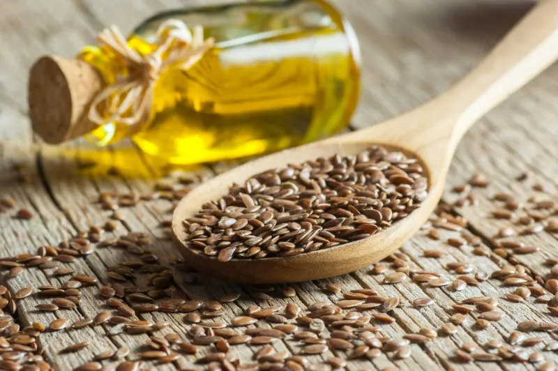 heap of flax seeds or linseeds in spoon and bowl with glass of linseed oil on wooden backdrop flaxseed or linseed concept flax seed dietary fiber