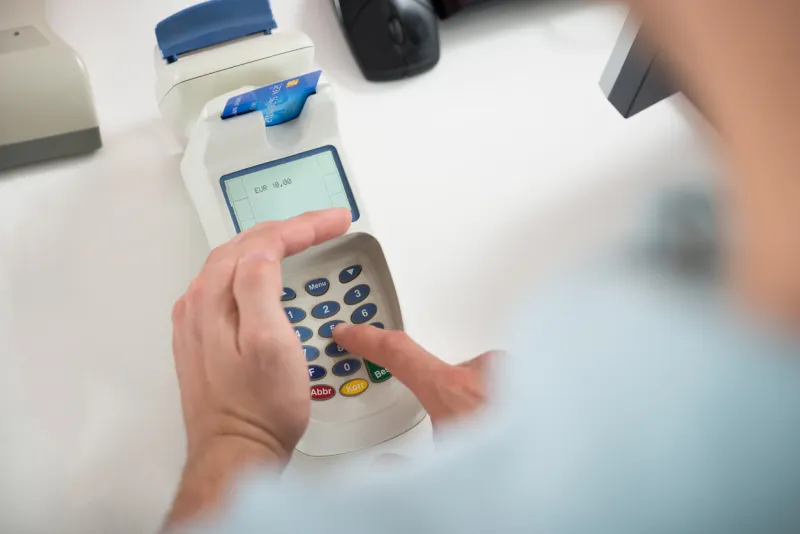 cropped image of male customer's hand entering pin code on card reader at clothing store