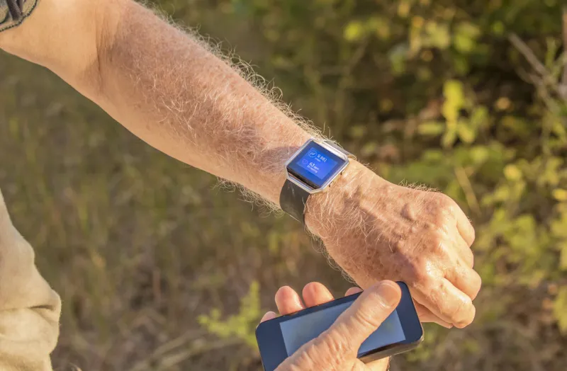 senior man checking his fitness information using his smart device and phone, grass in the background