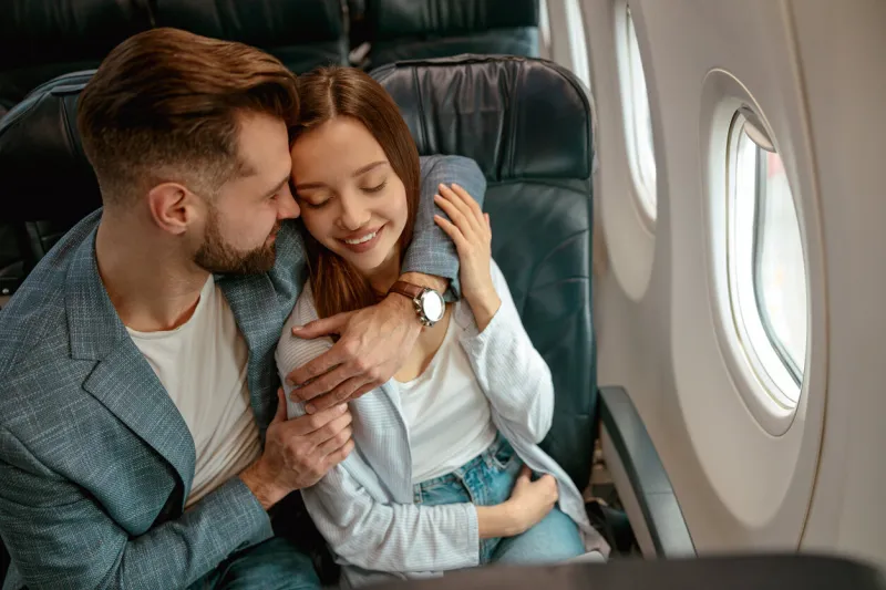 joyful woman sitting in passenger chair and smiling while loving man embracing her during flight