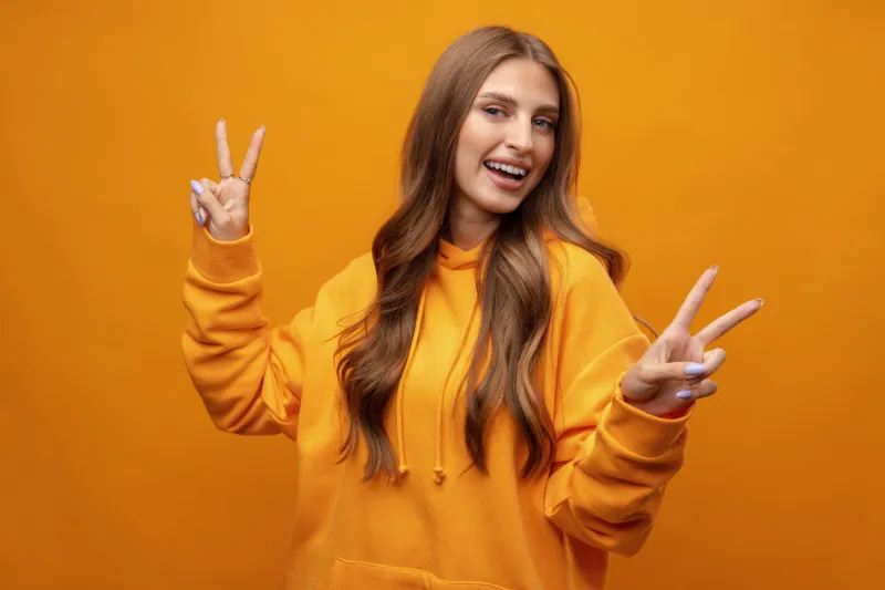 beautiful young woman with long hair doing victory sign on yellow background in studio