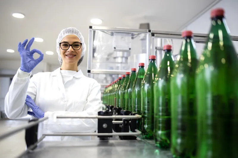 female technologist holding okay sign and approving production in beverage bottling factory