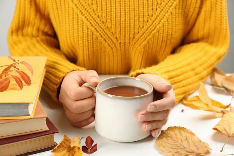 woman with cup of hot drink at white wooden table, closeup cozy autumn atmosphere