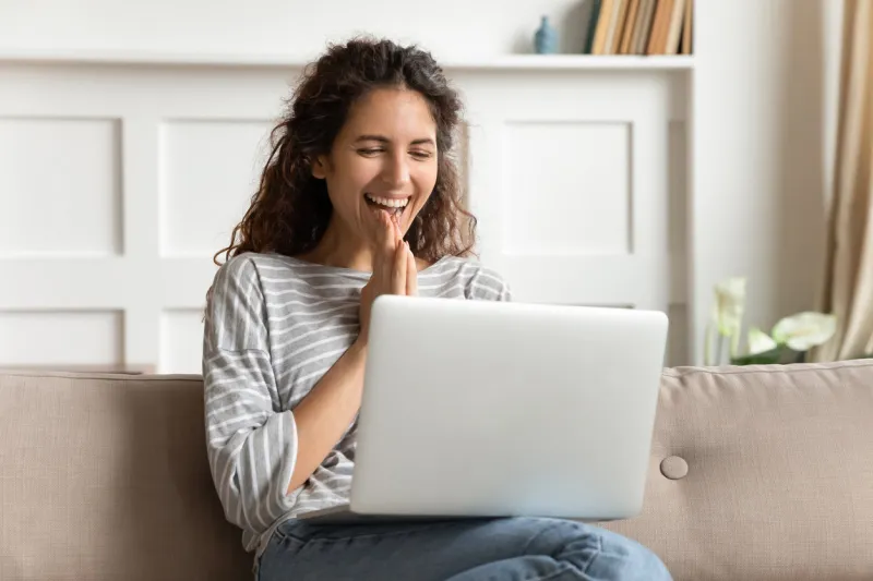 overjoyed young woman looking at laptop screen, feeling excited about good news at home happy attractive millennial lady received online lottery win notification, sitting on sofa in living room