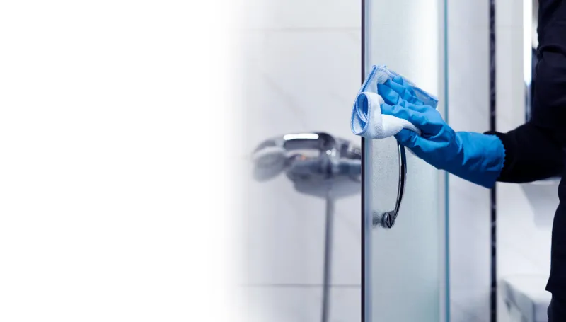 the maid's hand cleans the shower door in the bathroom with a copy space