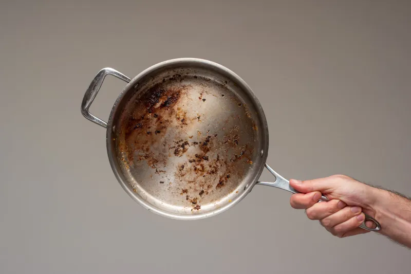 dirty oily burnt metal frying pan held in hand by male hand