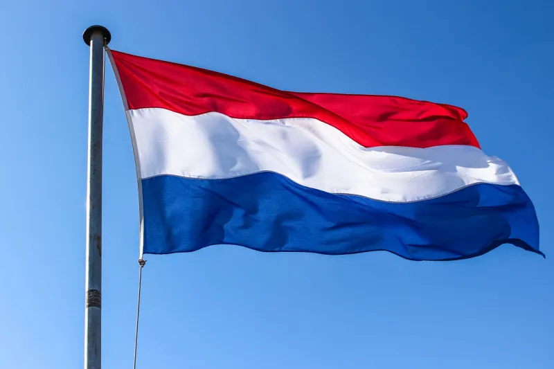 dutch flag on a flagpole waving in the wind, close up on a blue sky background