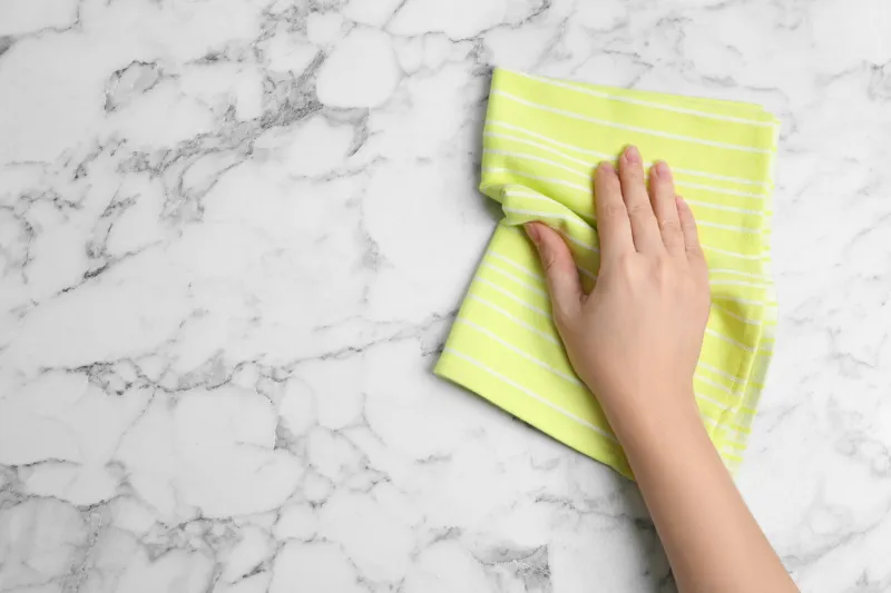woman wiping white marble table with kitchen towel, top view space for text
