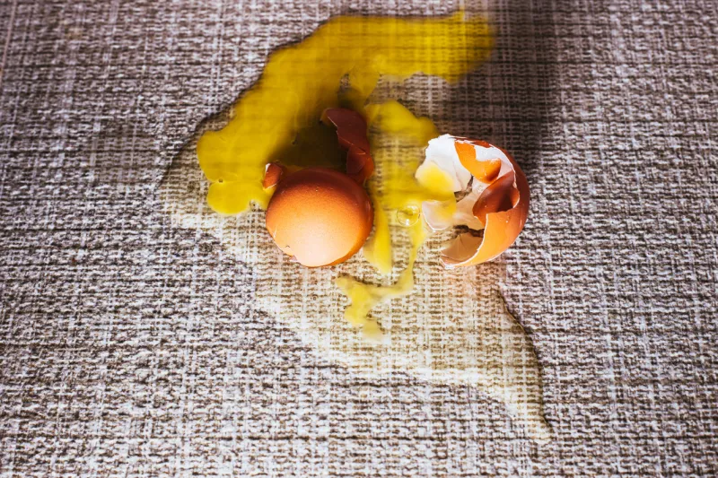broken egg on the floor on the tile - the egg shell and yolk spilled as a stain on the floor