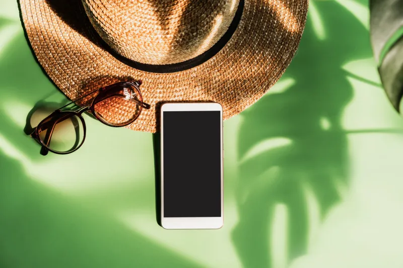 travel accessories and empty screen smart phone with shadow of tropical green leave on color background with copy space, summer vacation concept