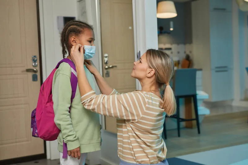 side view portrait of caring mother putting face mask on teen girl going to school, copy space
