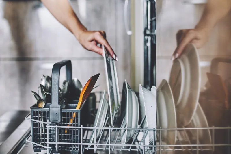 a woman's hand puts a dirty plate in the dishwasher