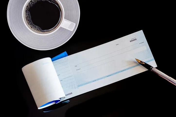 mockup image of checkbook, pen and white cup of coffee isolated on dark table background paycheque and payroll concept top view flat lay