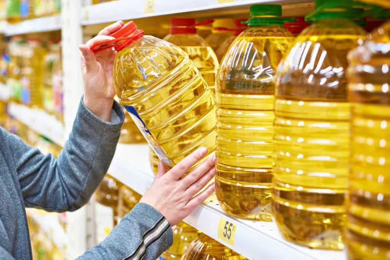 big plastic bottle of olive oil in the hand of the buyer at the grocery store