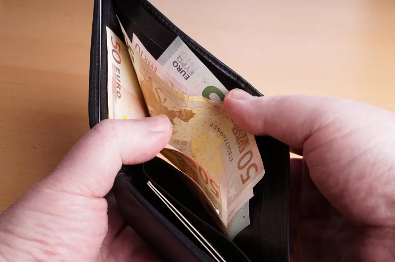 man opening black leather wallet full of euro bank notes