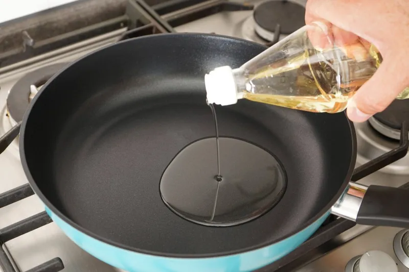 a man pours oil from a bottle into a frying pan in the kitchen close-up home cooking