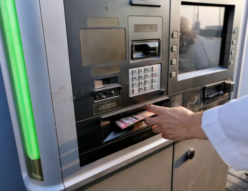 a white man's hand with long sleeve of arabian clothing taking money out from drivethru atm