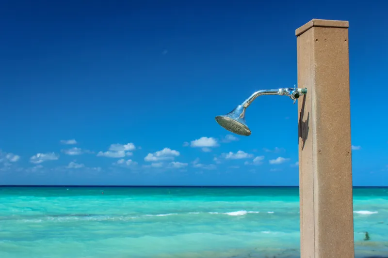 a shower station next to the ocean at a tropical beach - with vibrant skies and clear waters in the background, on a bright, sunny day