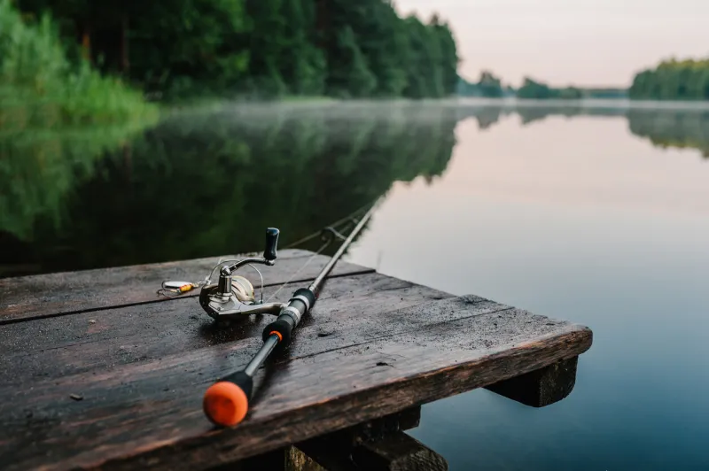 fishing rod, spinning reel on the background pier river bank sunrise fog against the backdrop of lake misty morning wild nature the concept of rural getaway article about fishing day