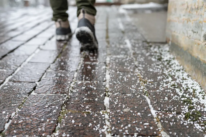 selective focus on technical salt grains on icy sidewalk surface in wintertime, used for melting ice and snow applying salt to keep roads clear and people safe in winter weather from ice or snow